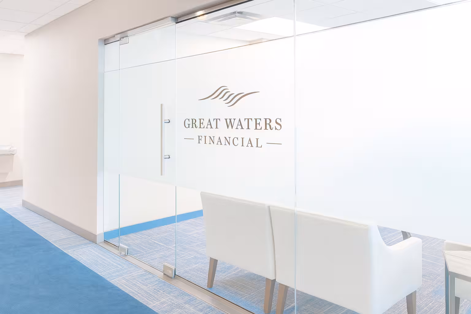 Office entrance with glass sliding door displaying Great Waters Financial logo and two white chairs inside.