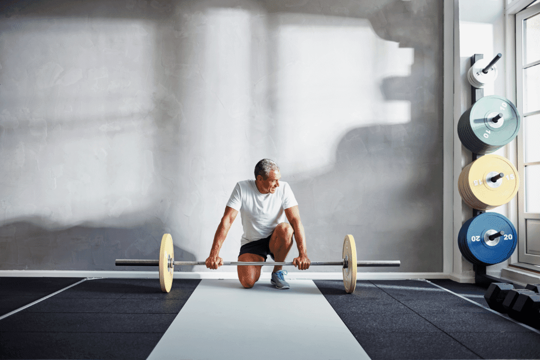 older man lifting weights alone in gym looking out window