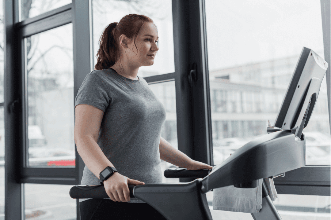 young woman on treadmill in gym next to large windows