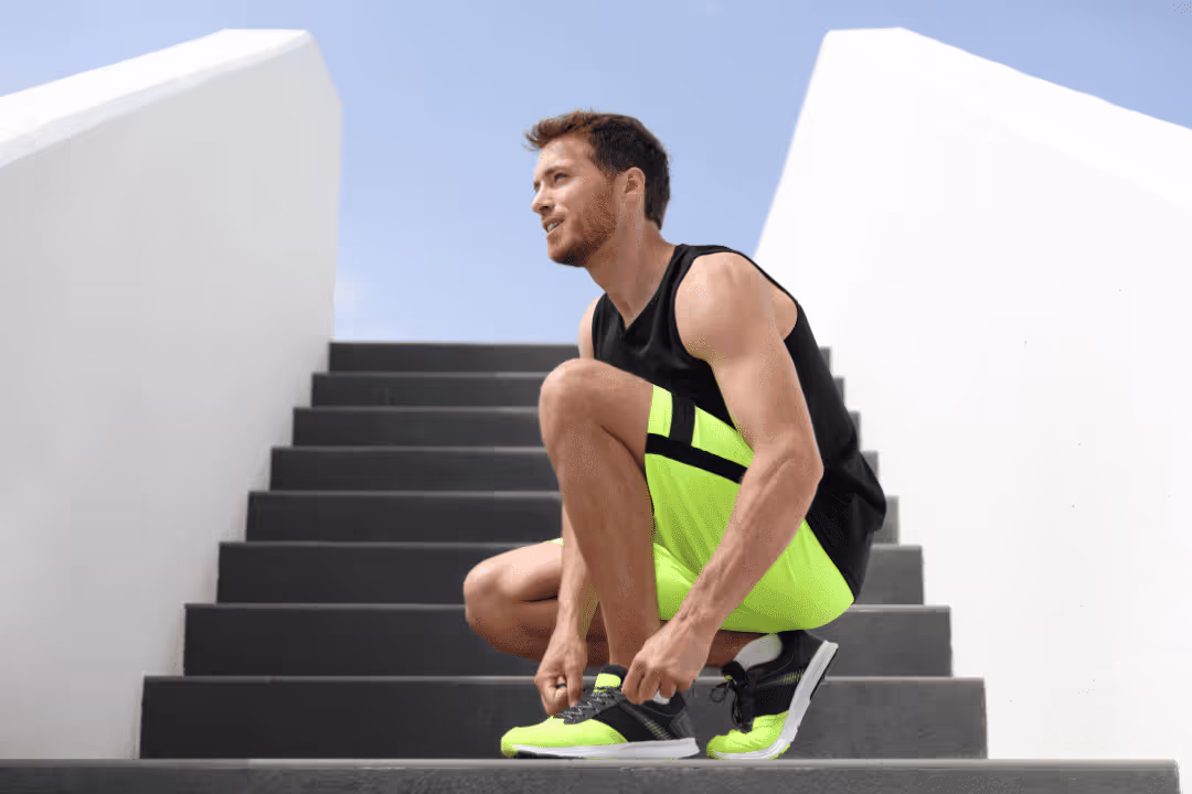 man lacing up neon running shoes neon shorts to run up stairs