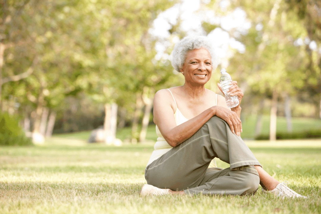 older woman holding water bottle workout clothes smiling sunny day park grass
