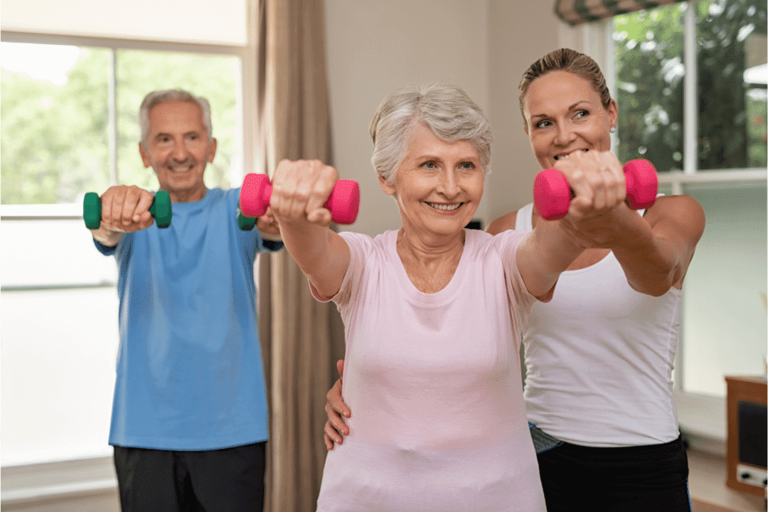 personal trainer helping older couple pink hand weights assistance smiling workout studio