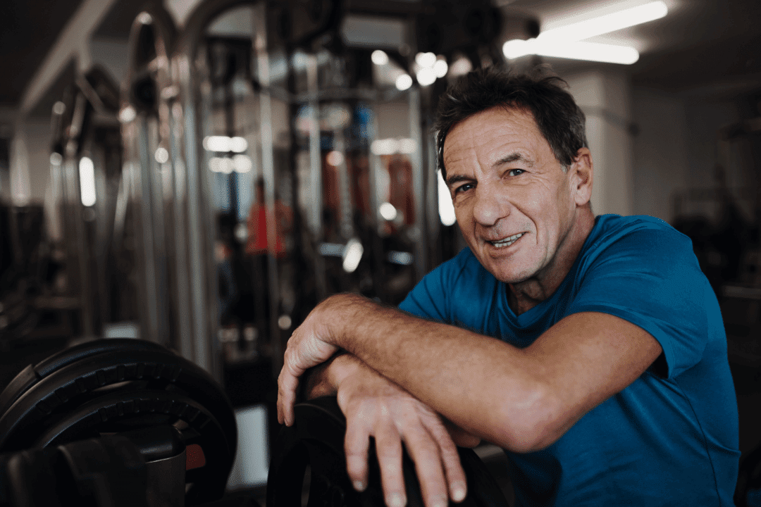 older man in gym looking at camera smiling accomplishment weight lifting machine