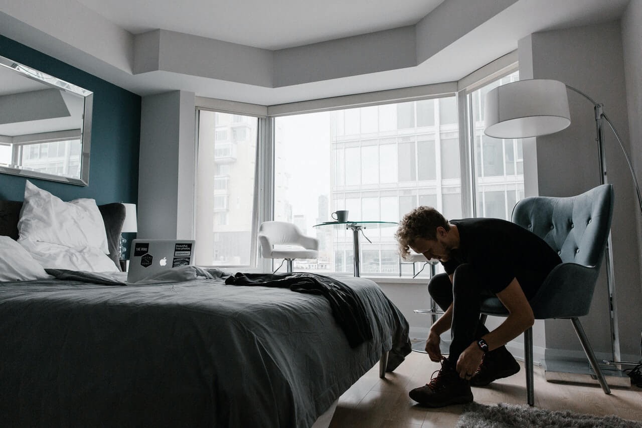 man in gray room tying shoes city morning run hotel bed lamp chair