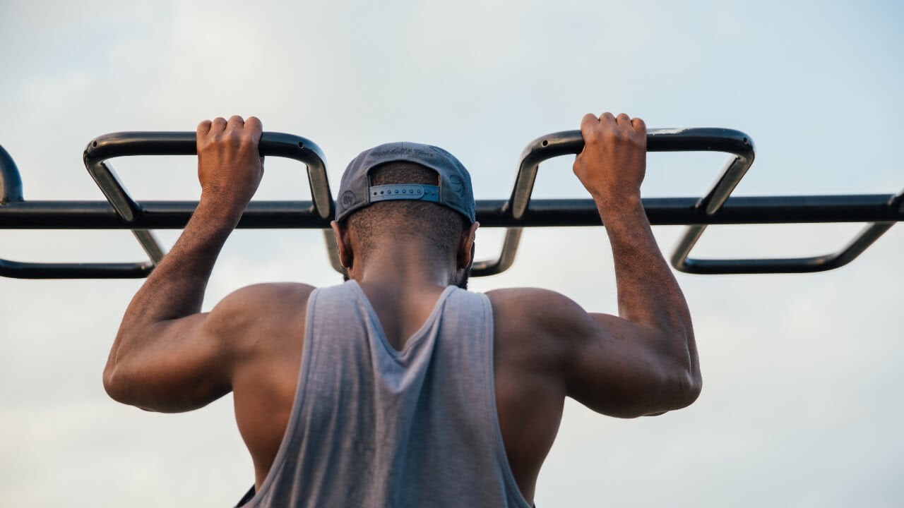 man pull up bar sky exercise arms tank top snapback hat