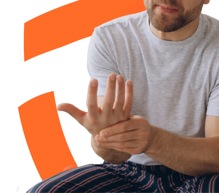 Bearded man in a grey t-shirt and striped pajama pants massaging his left wrist with his right hand.