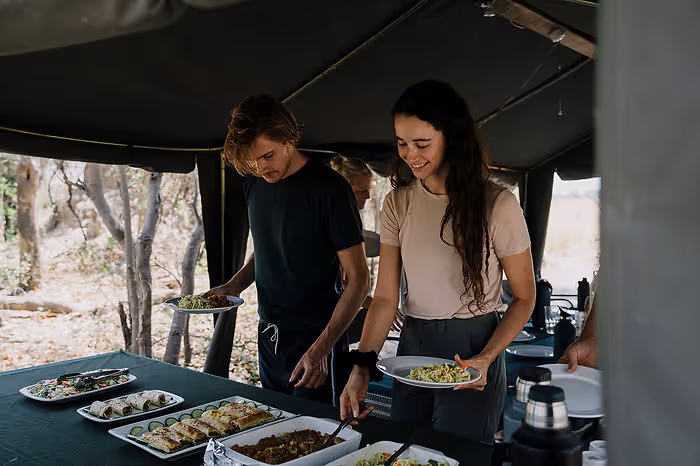 A man and woman serve themselves food in a tent