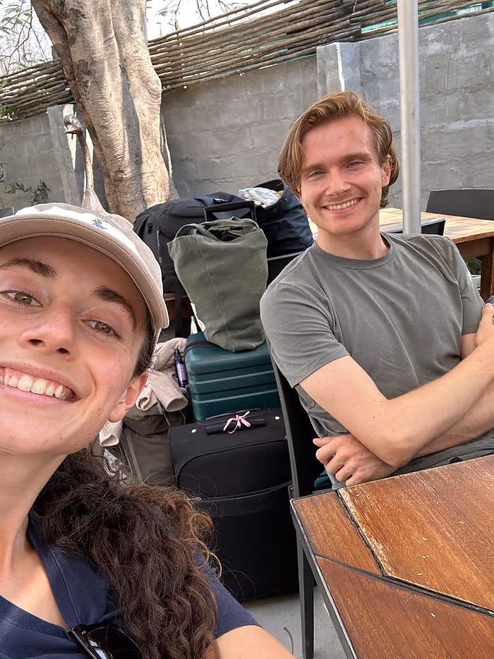A man and woman smiling at a camera with bags and suitcases behind them.