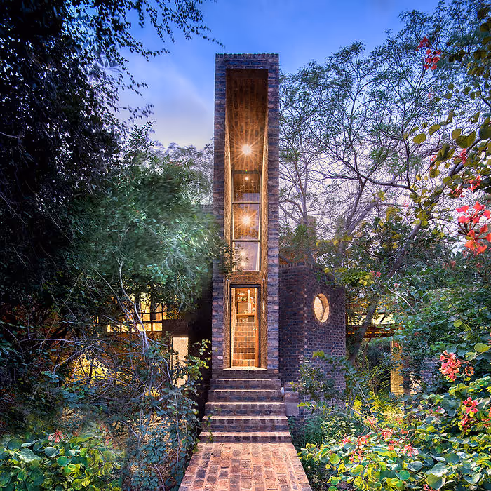 very skinny house made of brick surrounded by lush greenery