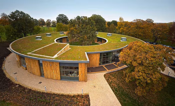 round modern house covered with green roof and surrounded by trees