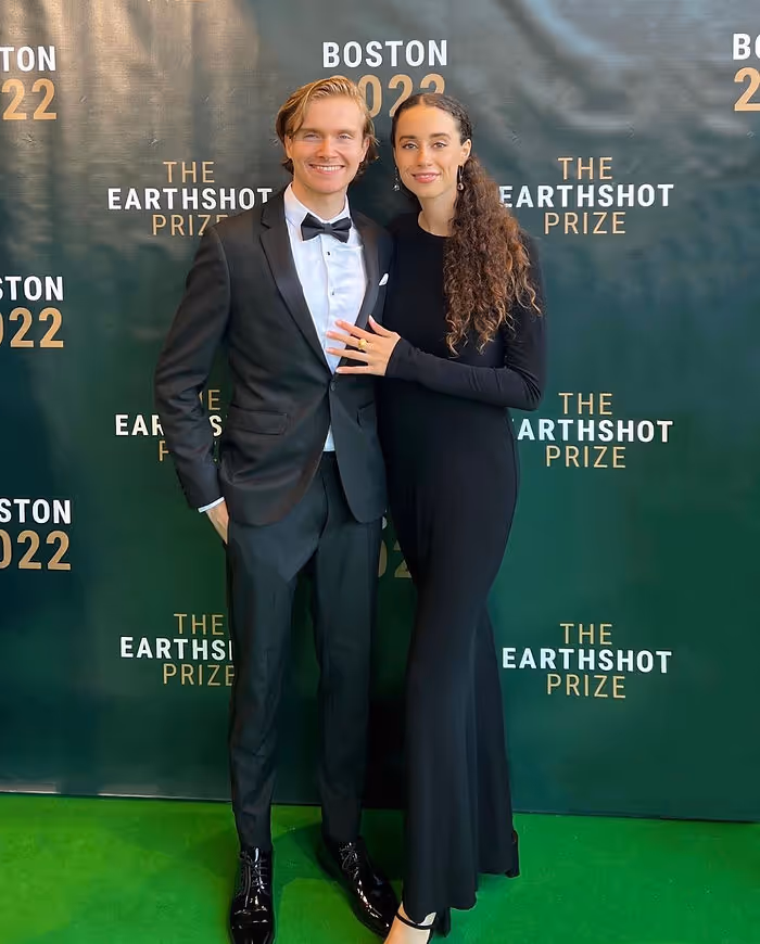 man and woman standing in front of green wall on green carpet in tuxedo and gown