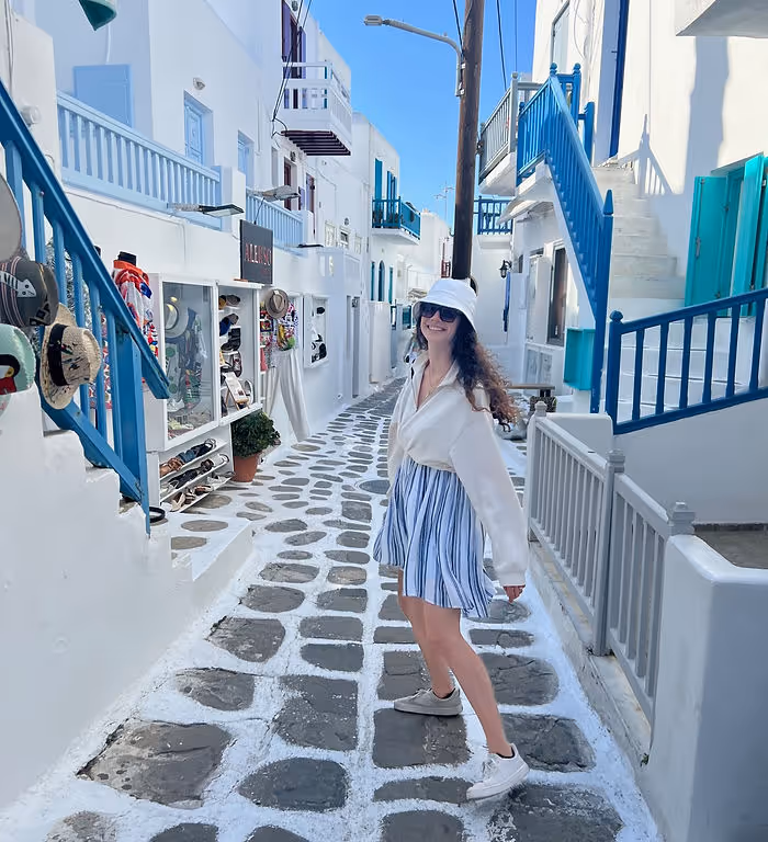 woman walking along cobblestone streets of Mykonos with blue railings and white walls along the sides