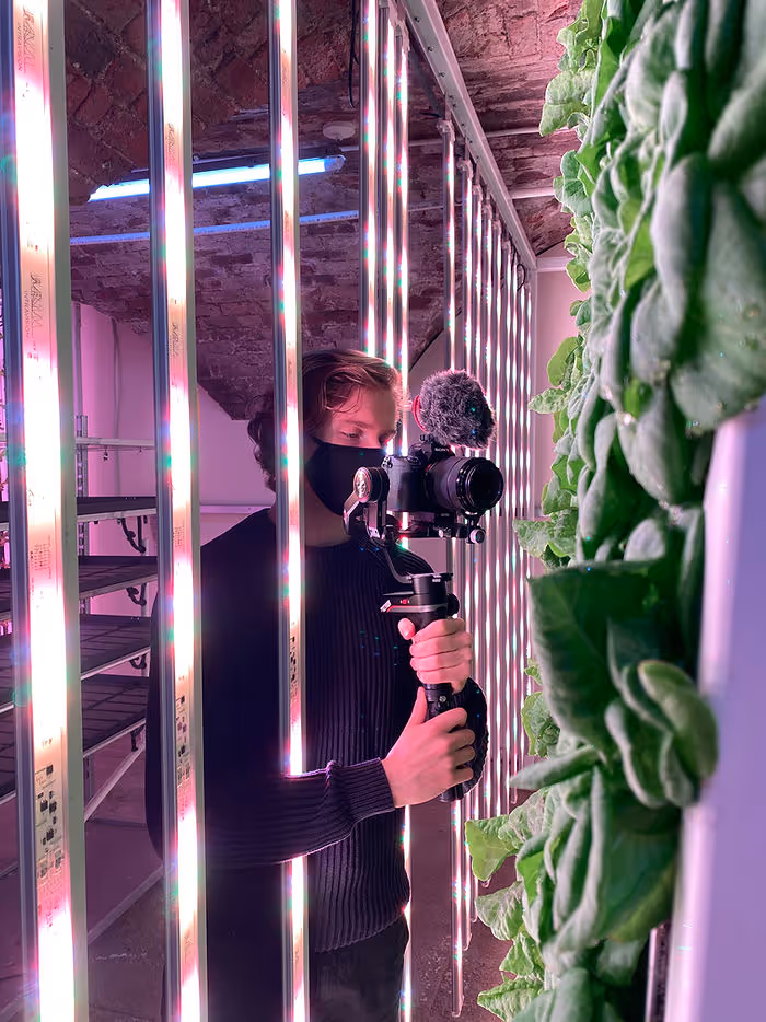 man holding camera pointed at produce grown in vertical farm