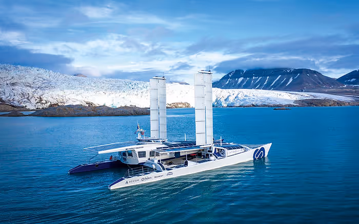 large wind-powered boat in front of glacier