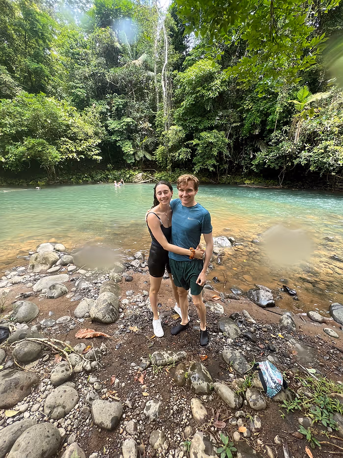 A man and woman standing on a riverbank smiling and embracing.
