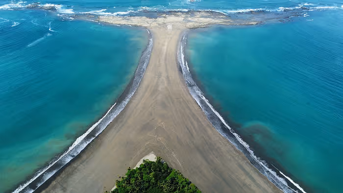 A stretch of sandy beach in the shape of a whale's tail surrounded by bright blue water.