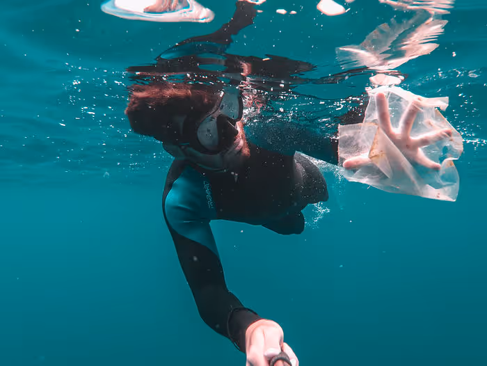 A man scuba diving in the ocean surrounded by plastic.