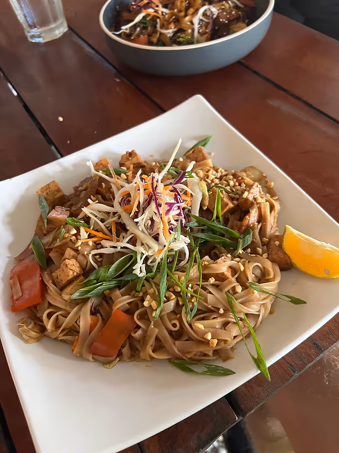 A plate of noodles with different vegetables and a lemon slice.
