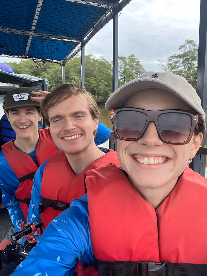 Three people in red life jackets smile at the camera on a boat.