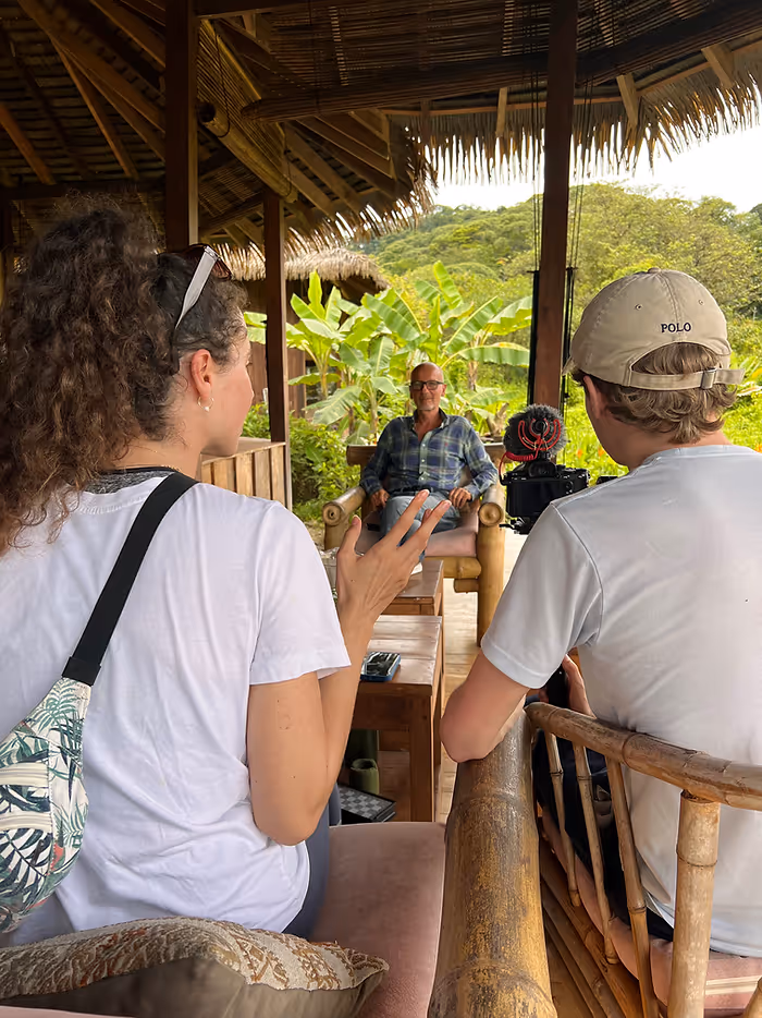 A man sitting in between another man and a woman with a camera, interviewing him.
