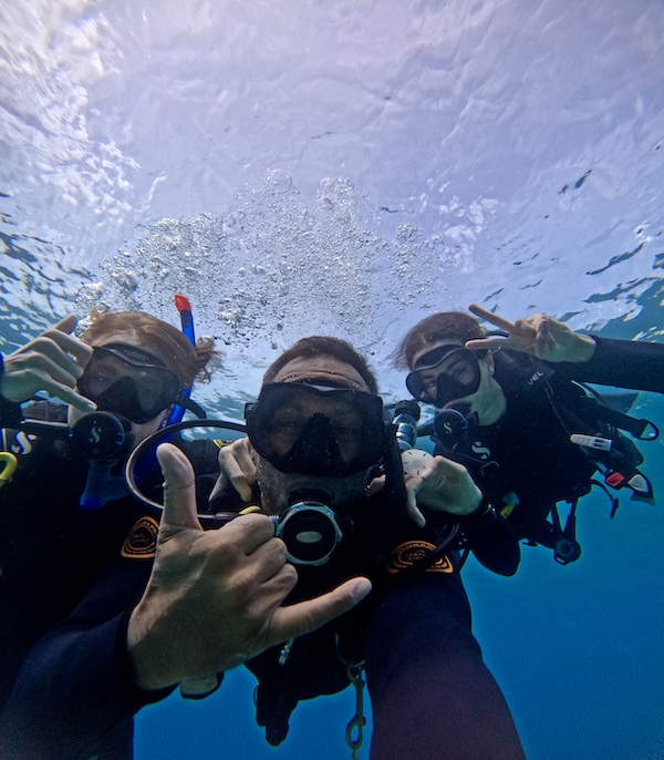 three scuba divers with masks taking a selfie