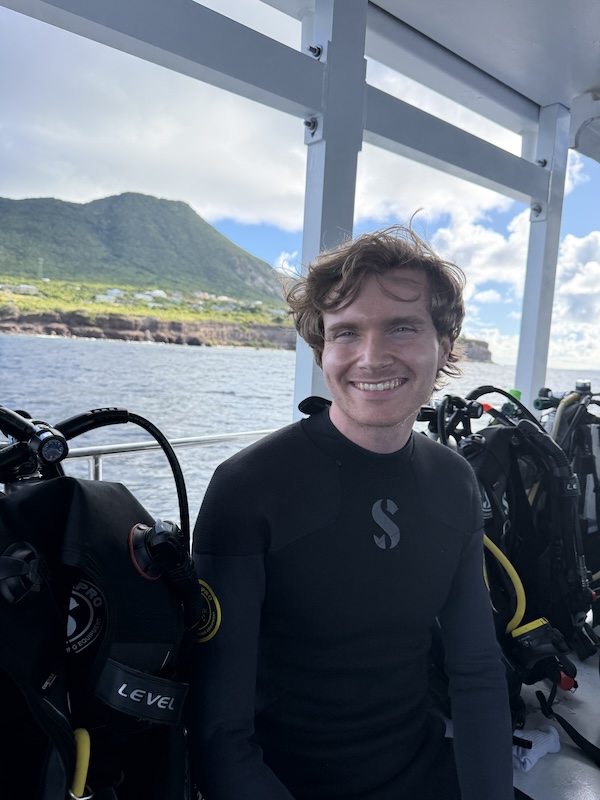 man in wetsuit sitting on a boat smiles