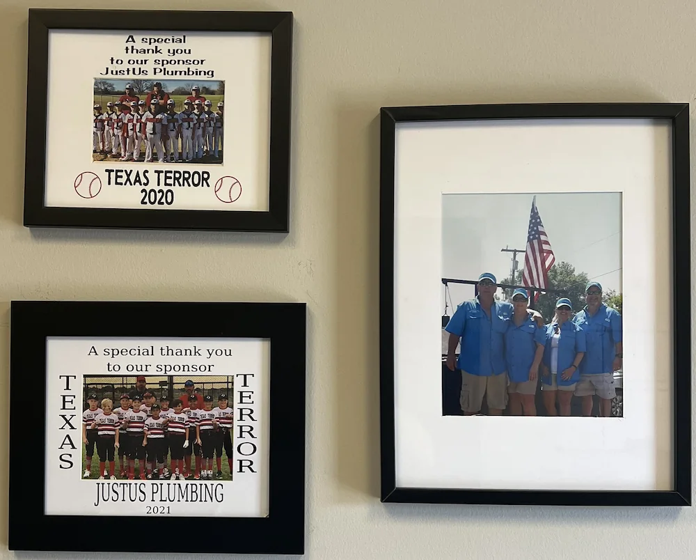 Three framed photos on a wall: two team photos of youth baseball teams labeled Texas Terror 2020 and 2021 thanking sponsor JustUs Plumbing, and one photo of four adults in blue shirts standing in front of an American flag.