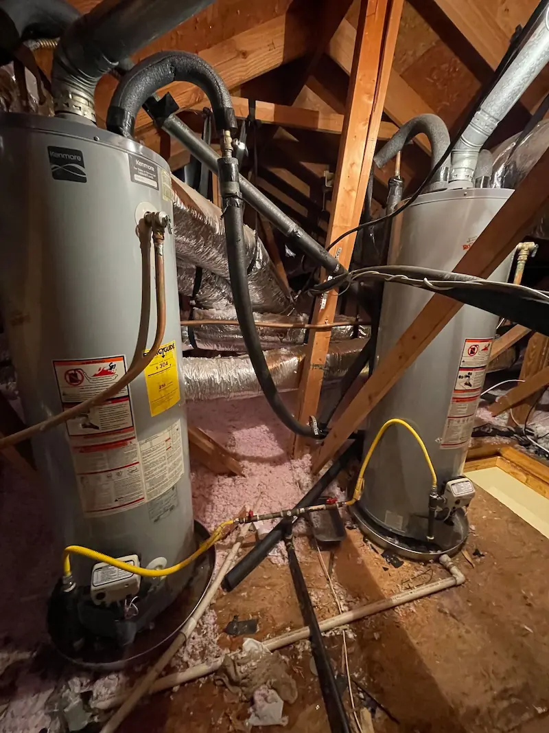 Two gray Kenmore water heaters installed in an attic with exposed wooden beams and insulation.