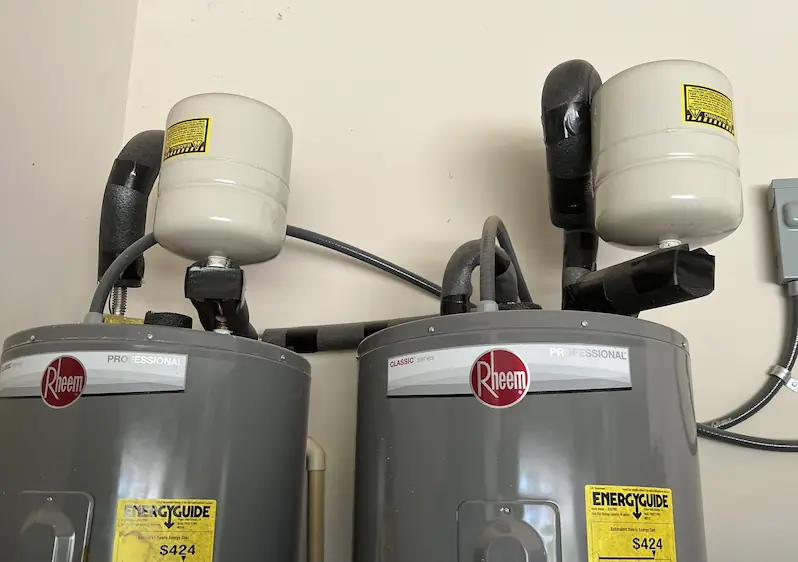 Two outdoor water meters partially covered with fallen leaves inside a meter box.