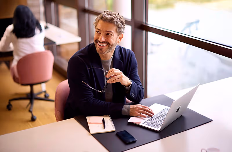 A confident man in office using an Apple laptop