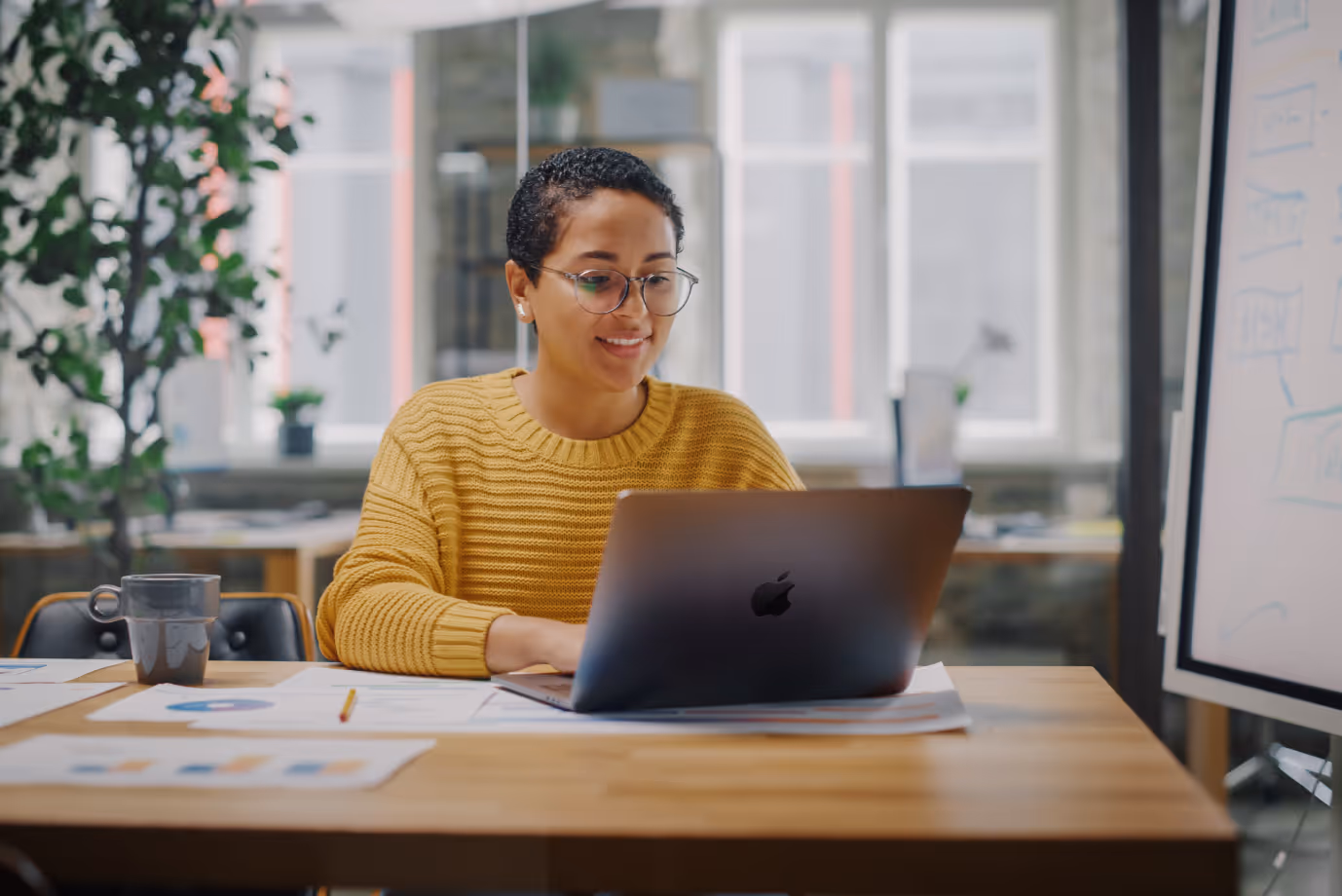 A woman in a bright yellow jumper using a laptop in a meeting room