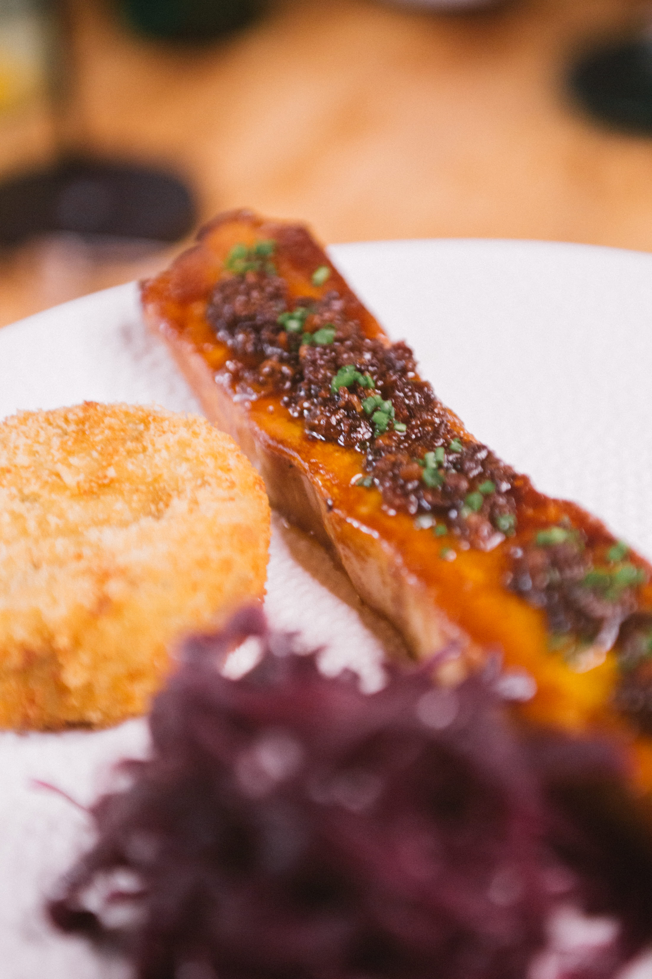 Ein Gericht aus Schweinebauch, Kartoffel-Käse- Rösti und Rotkraut in Nahaufnahme auf einem Teller