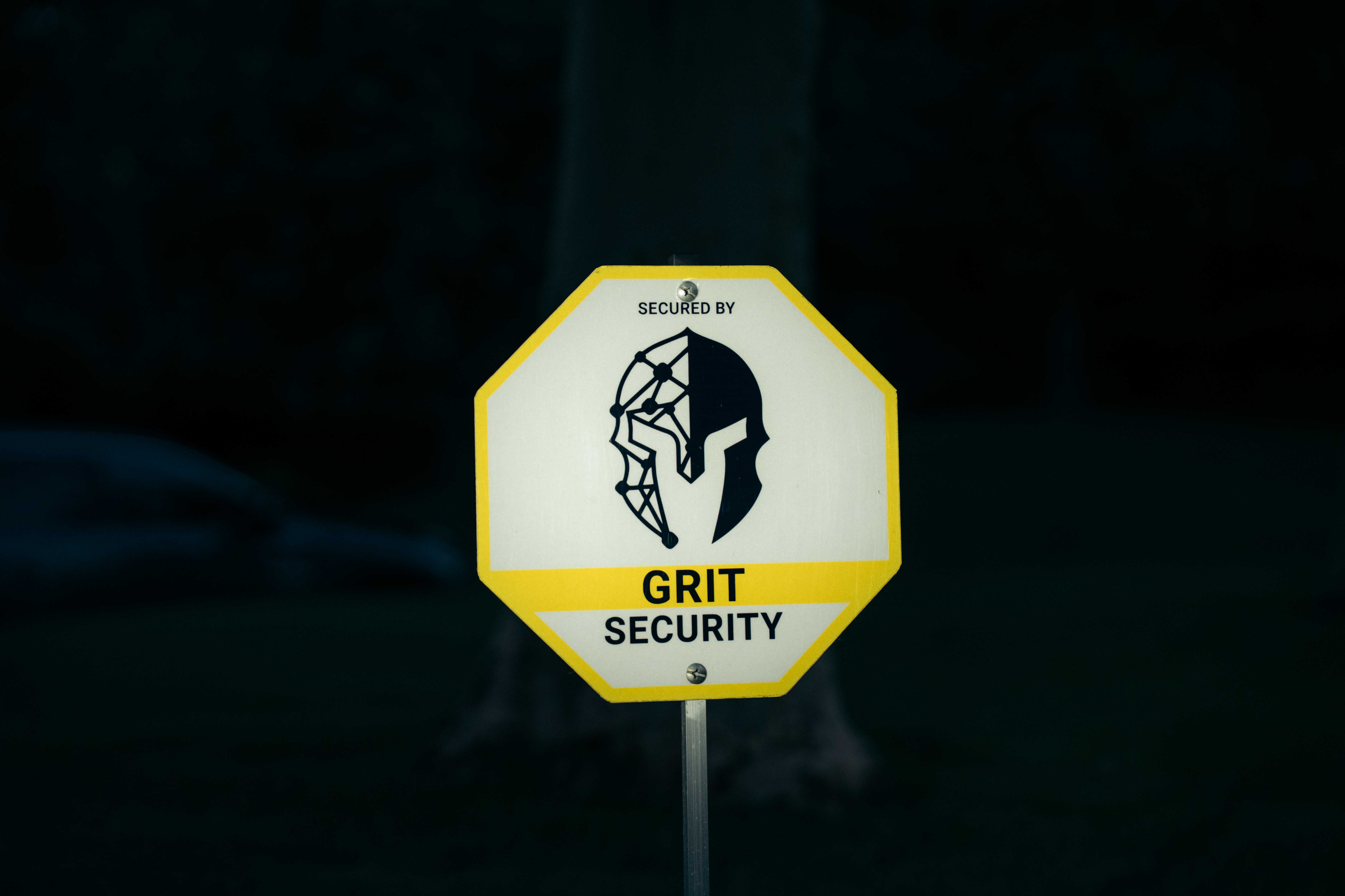 Yellow bordered security sign reading 'Secured by GRIT Security' with a half robotic, half Spartan helmet logo.