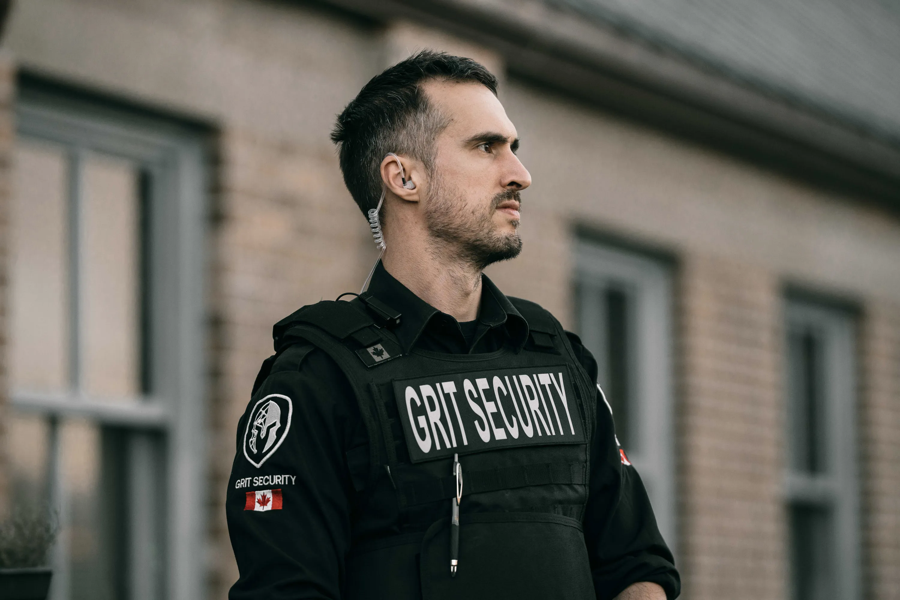 Security guard wearing a black uniform and bulletproof vest labeled 'GRIT SECURITY' with a Canadian flag patch.