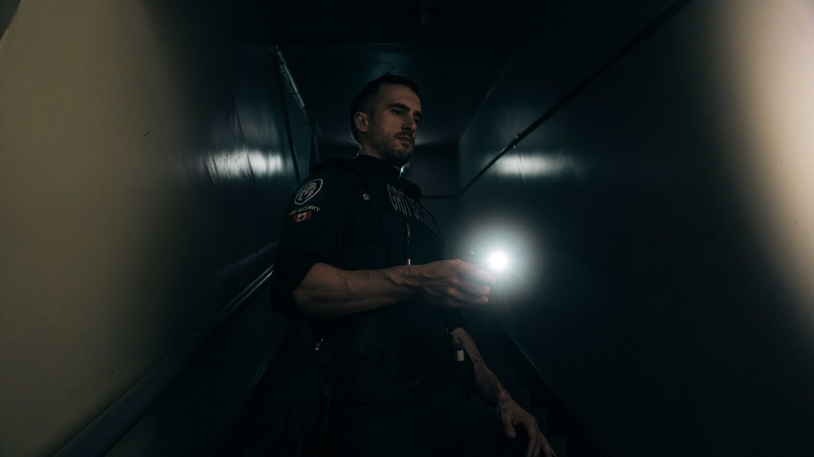 Uniformed Grit Security officer conducting a flashlight patrol in a dim interior corridor.