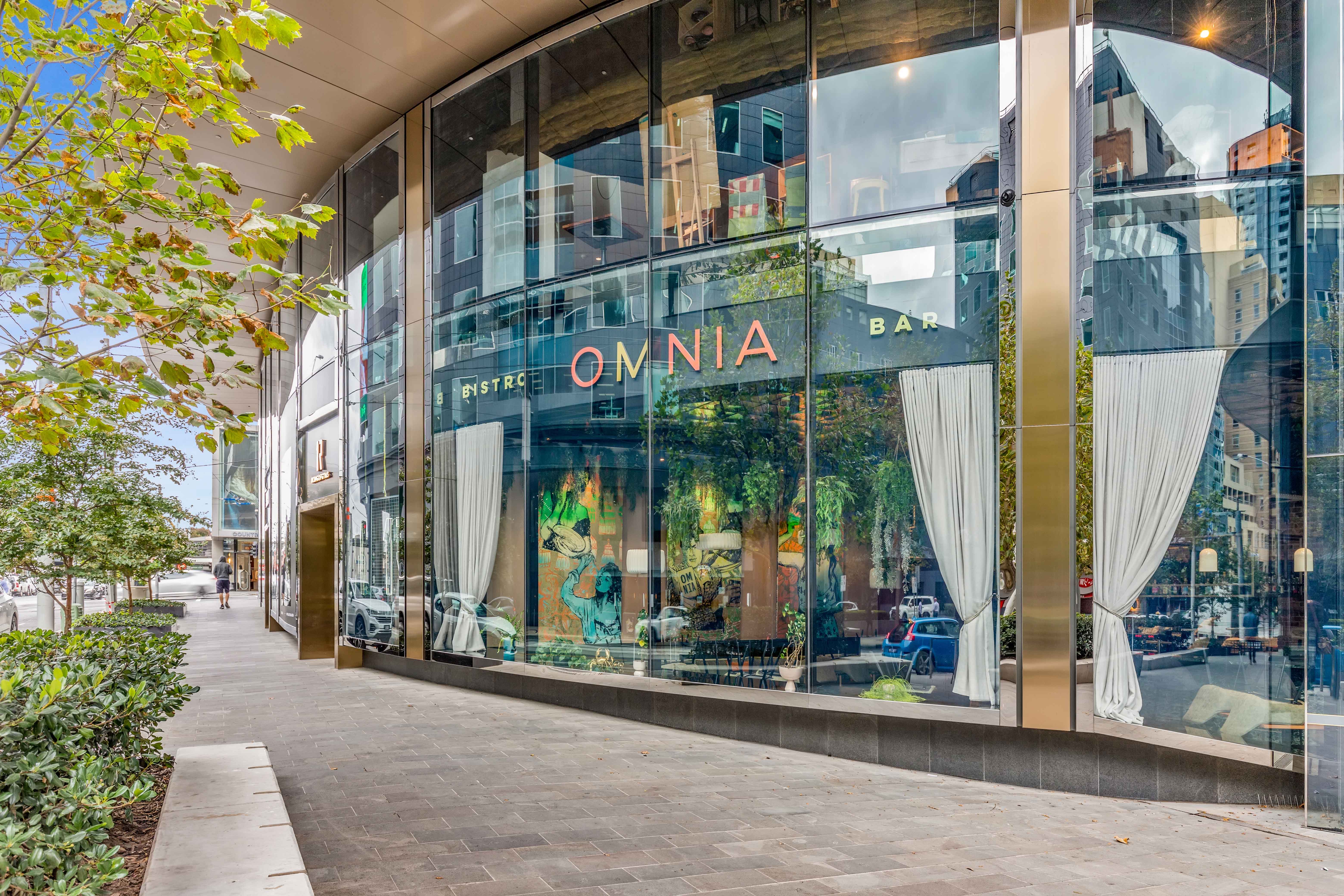 Street view of Omnia Bistro Bar with large glass windows reflecting city buildings and trees.