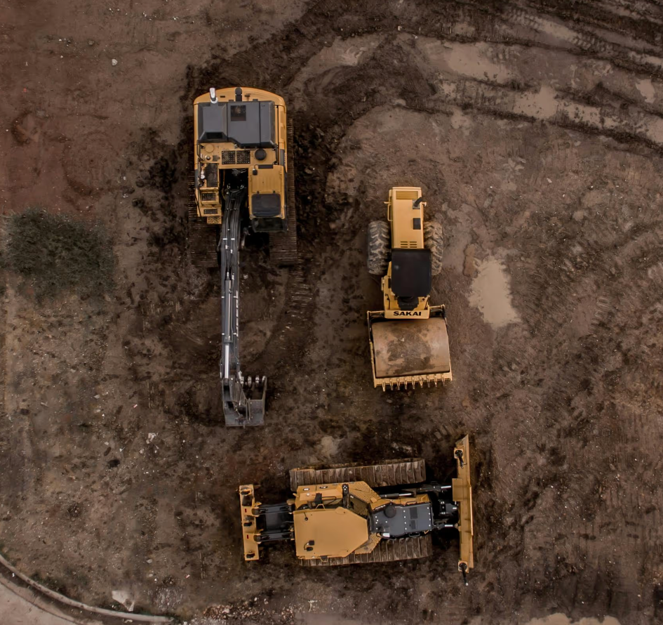 Aerial view of three yellow construction vehicles on muddy ground forming a smiley face.