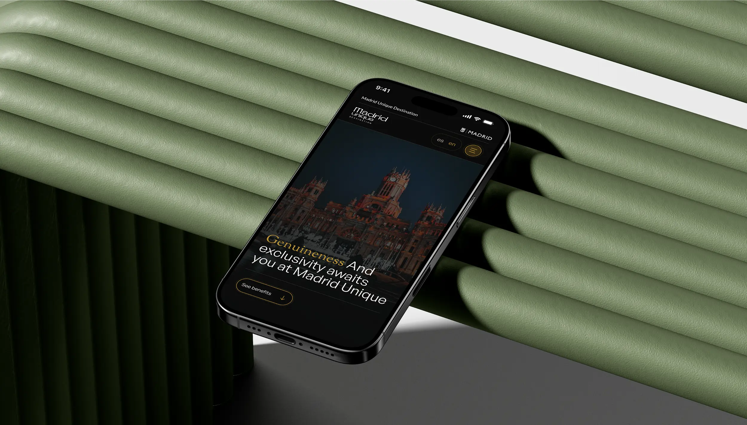 Smartphone displaying Madrid Unique Destination website with text about genuineness and exclusivity, on a textured green cylindrical and tubular background.