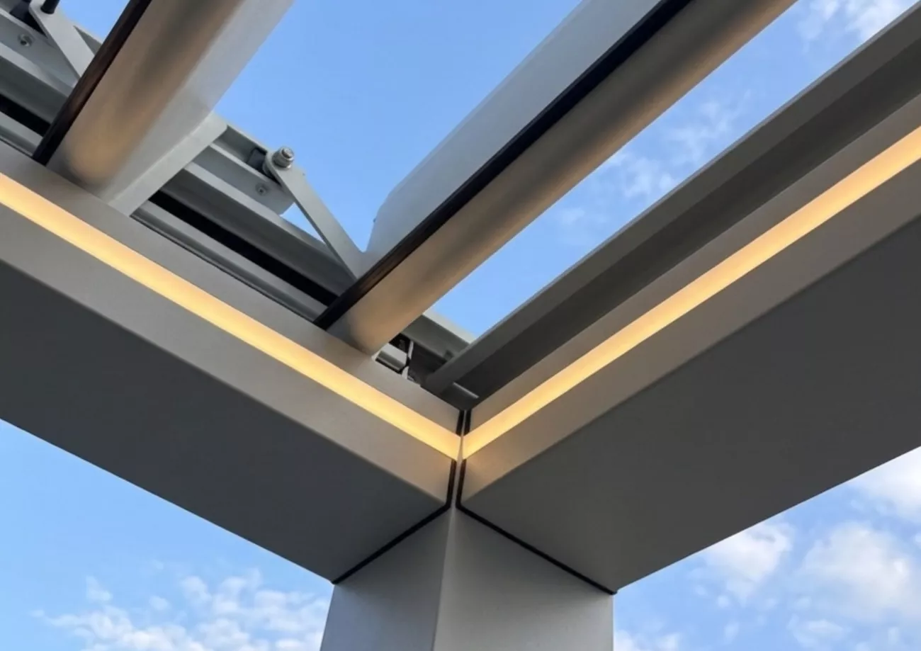 Aluminium pergola corner post with warm LED perimeter lighting and open tilting louvre roof panels.