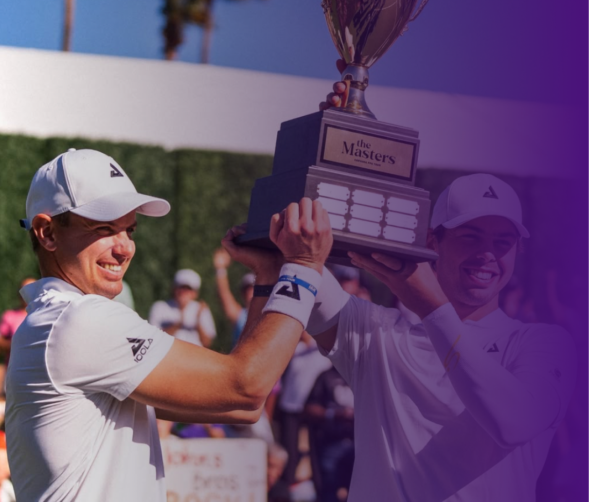 Two male athletes in white sportswear smiling and holding up a large trophy labeled "The Masters" in celebration.