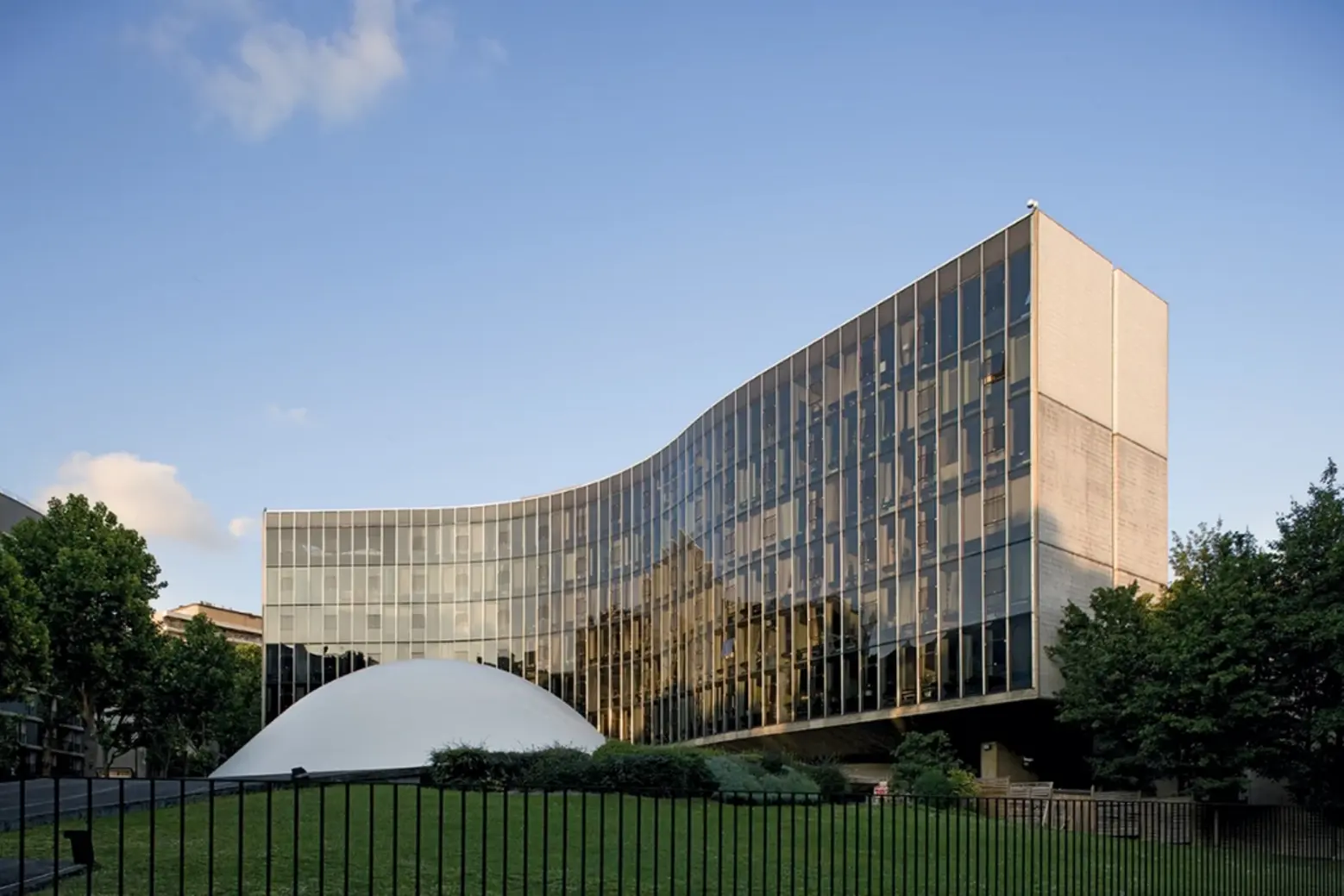 The top of the auditorium dome rises in front of party secretariat, an undulating six-story slab, its steel-and-glass curtain wall designed by Jean Prouvé Espace Niemeyer
