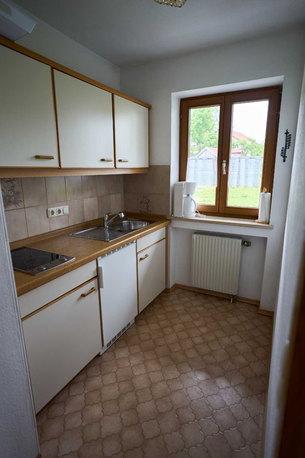 Kleine Küche mit Holzarbeitsplatte, Spüle, Herd, weißen Schränken und Fenster mit Kaffeeautomat und Küchenrolle.