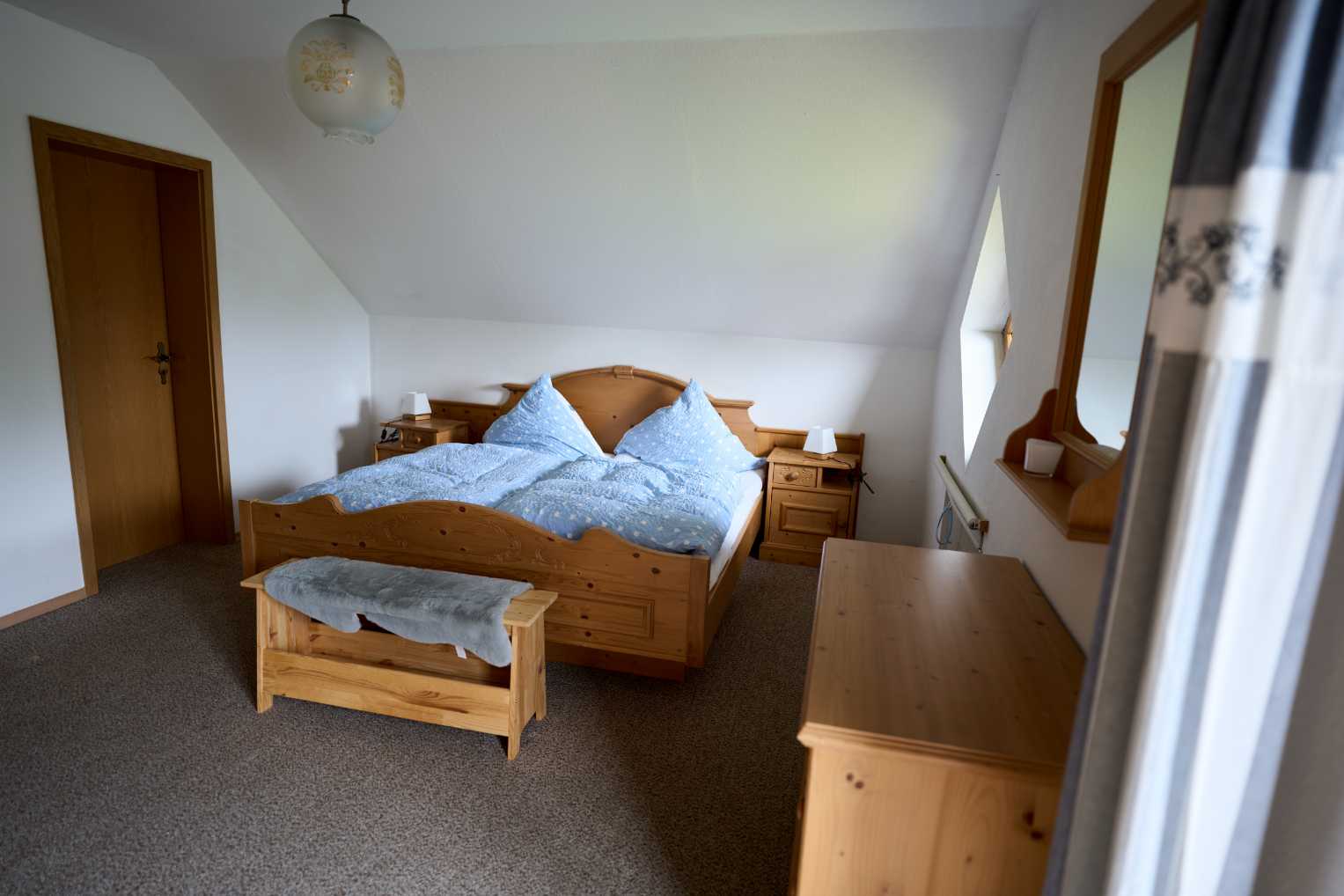 Schlafzimmer mit Holzmöbeln, Doppelbett mit blauer Bettwäsche und zwei Nachttischen mit Lampen.