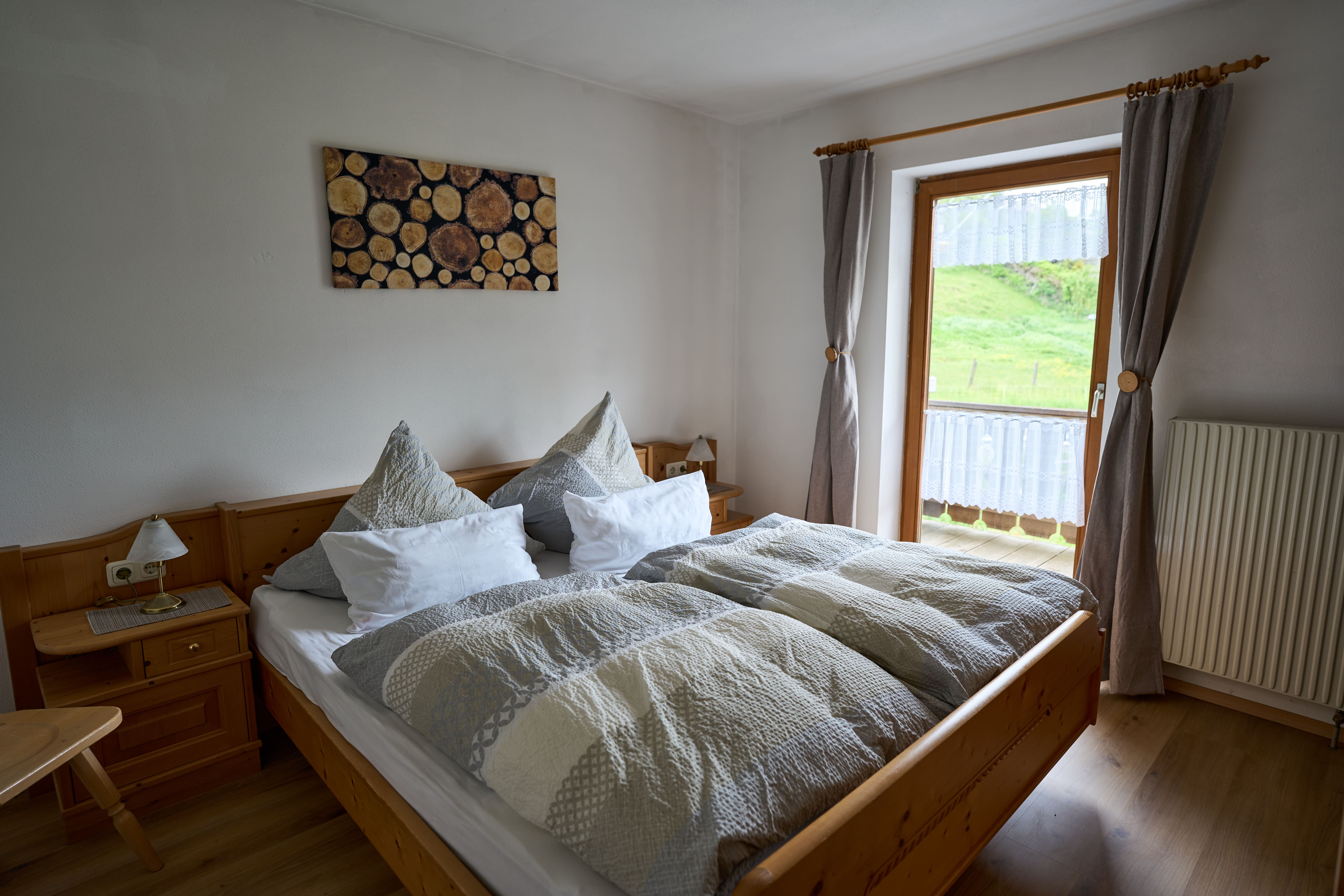 Hell eingerichtetes Schlafzimmer mit Doppelbett, Holzmöbeln und Balkonblick auf eine grüne Landschaft.
