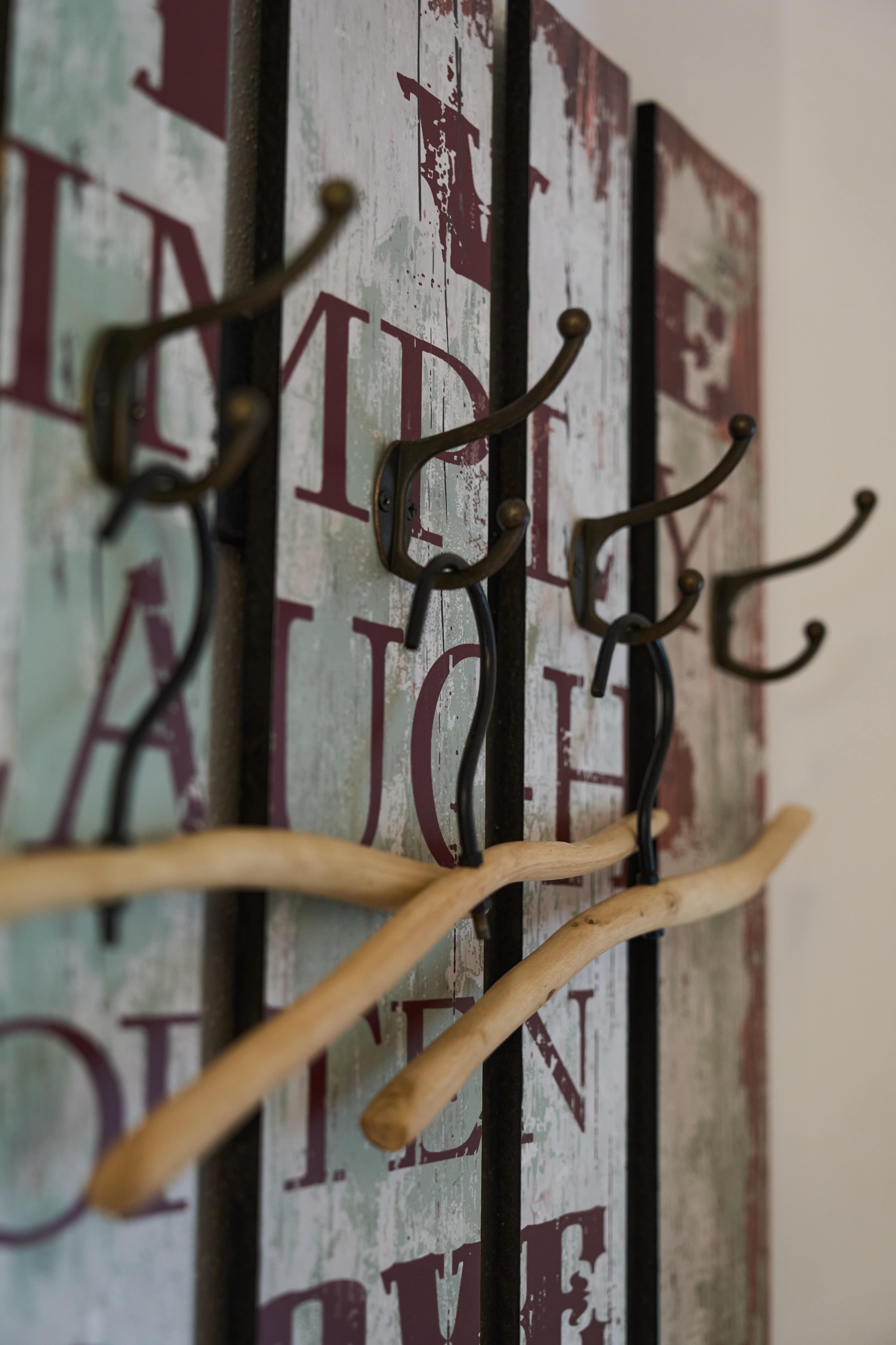 Mehrere Holzbügel hängen an Metallhaken an einer vintage Wanddekoration mit verblasstem Schriftzug.