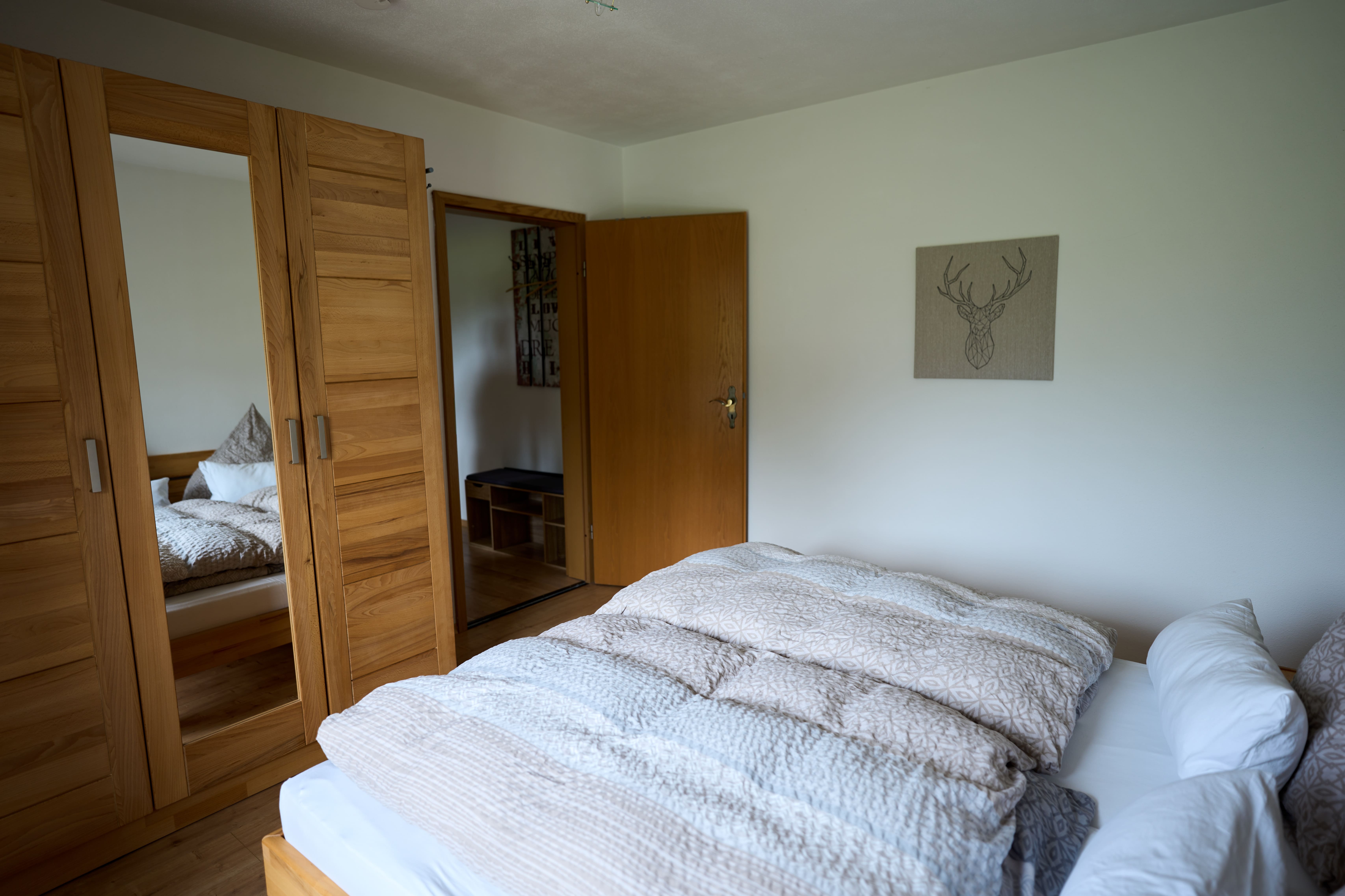Schlafzimmer mit einem großen Bett mit gemusterten Bettdecken, einem Holzkleiderschrank mit Spiegel und einer offenen Holztür.