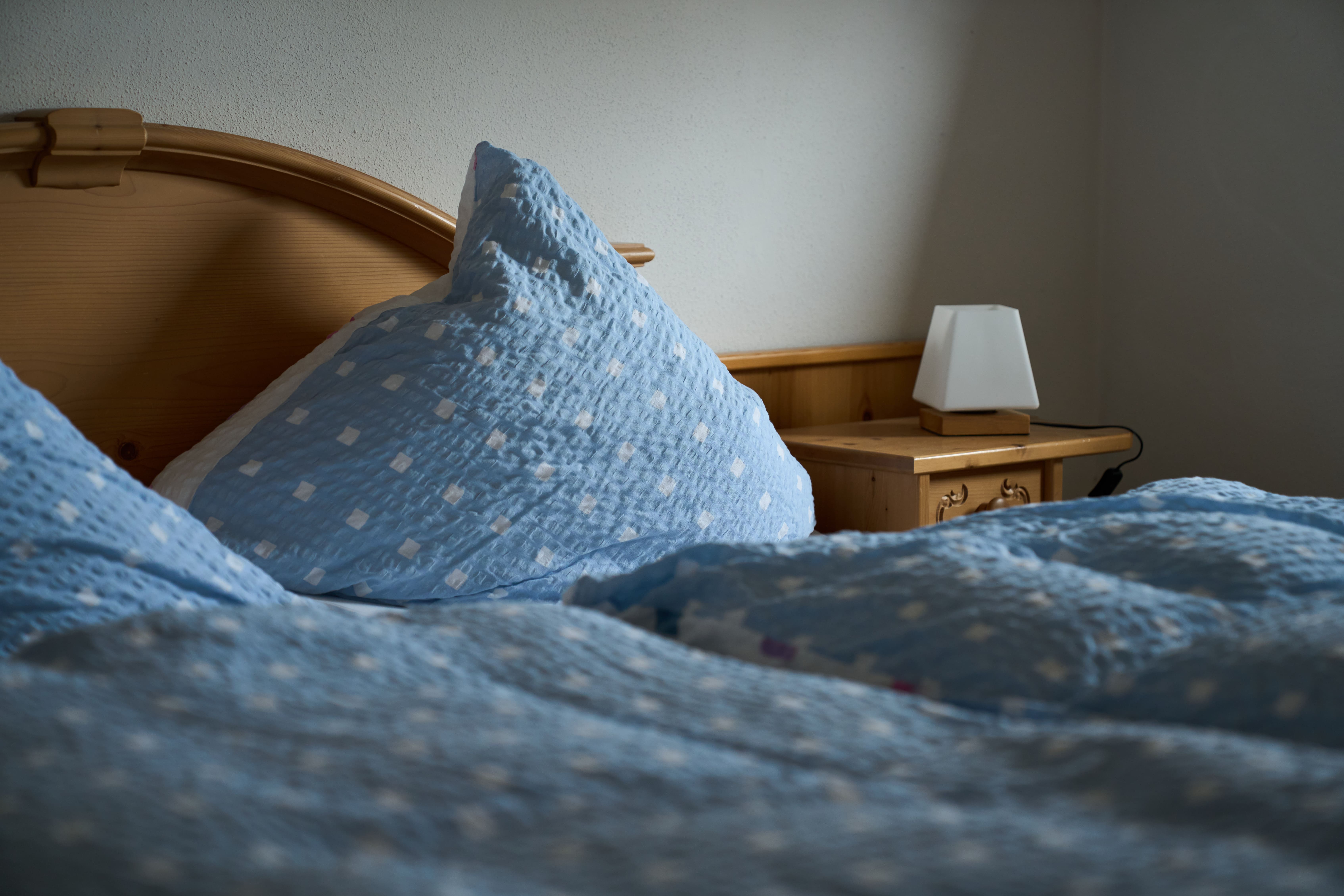 Nahaufnahme eines Bettes mit blauer, gepunkteter Bettwäsche und einem Nachttisch mit weißer Lampe.