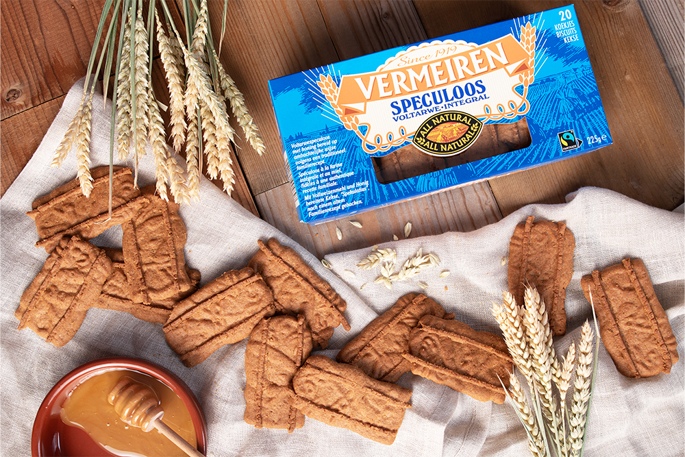 Gestapelde Vermeiren Voltarwspeculoos op een doek, met graan, honing en de verpakking erbij