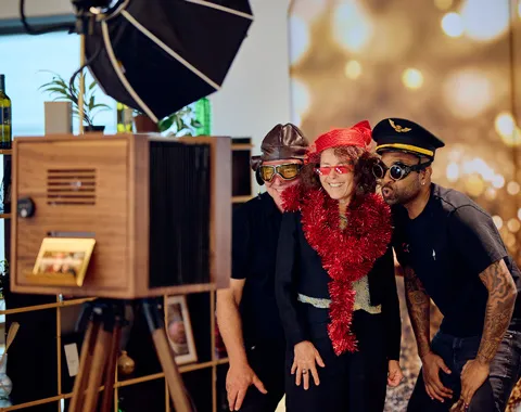 Drei Personen verkleidet mit lustigen Accessoires posieren für ein Foto vor einer Fotobox.
