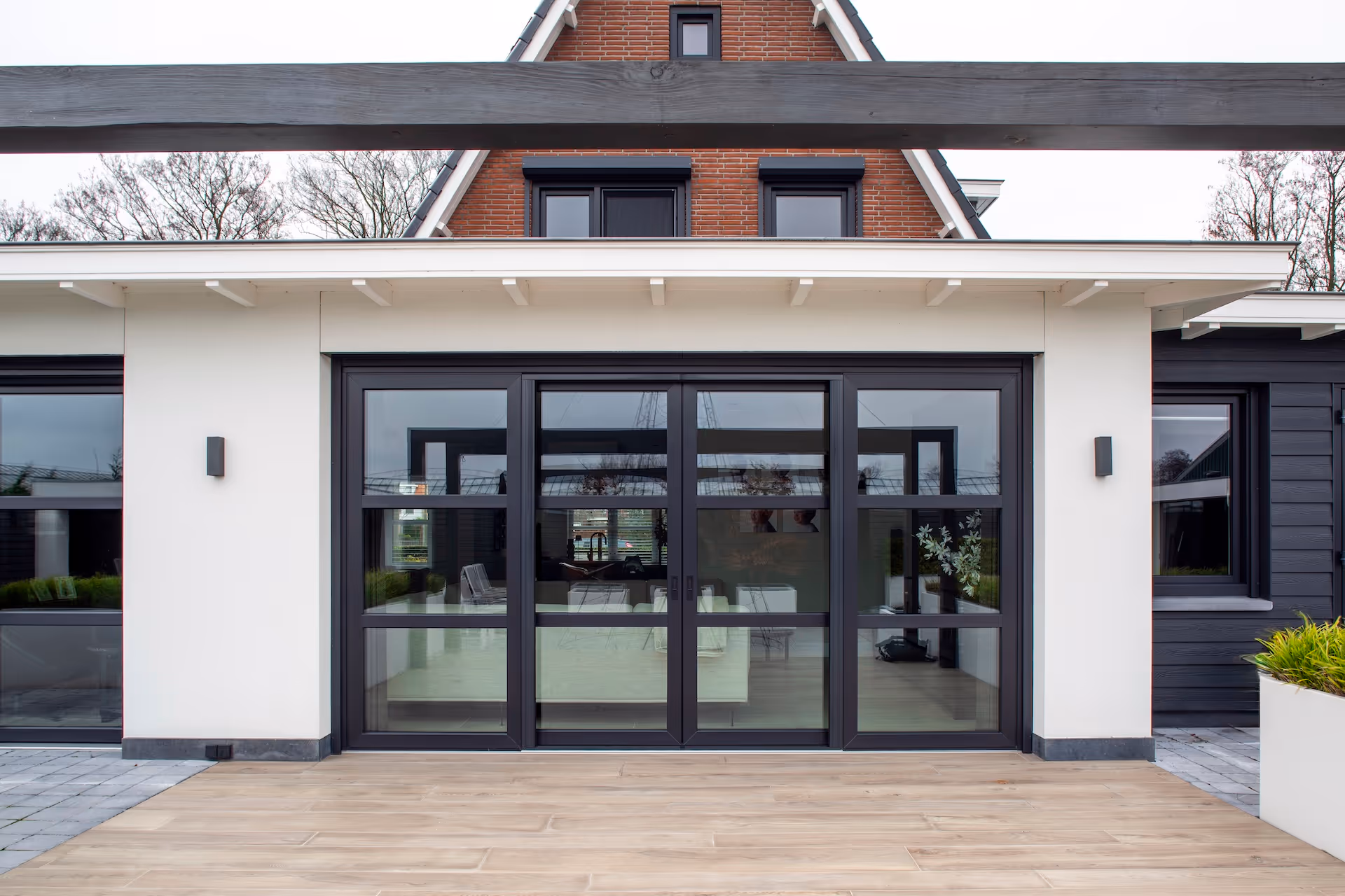 Moderne woonhuis gevel met grote glazen schuifdeuren met zwarte frames en witte muren.
